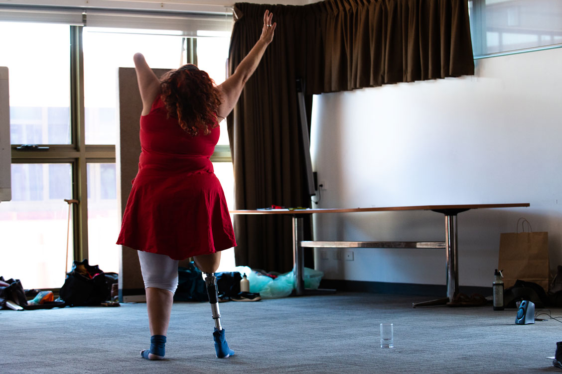 Artist participant standing on a prosthetic leg and rising hands 